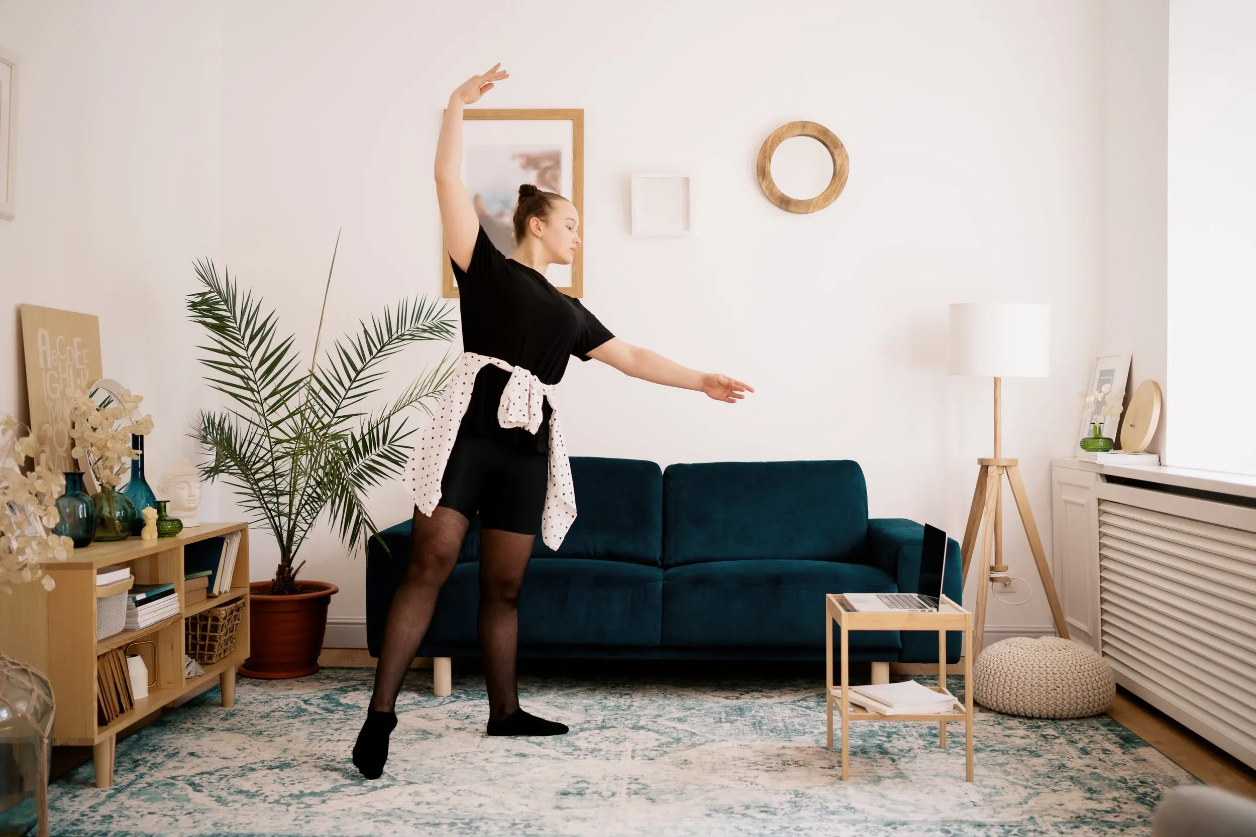 A teenager practicing ballet with a laptop at home